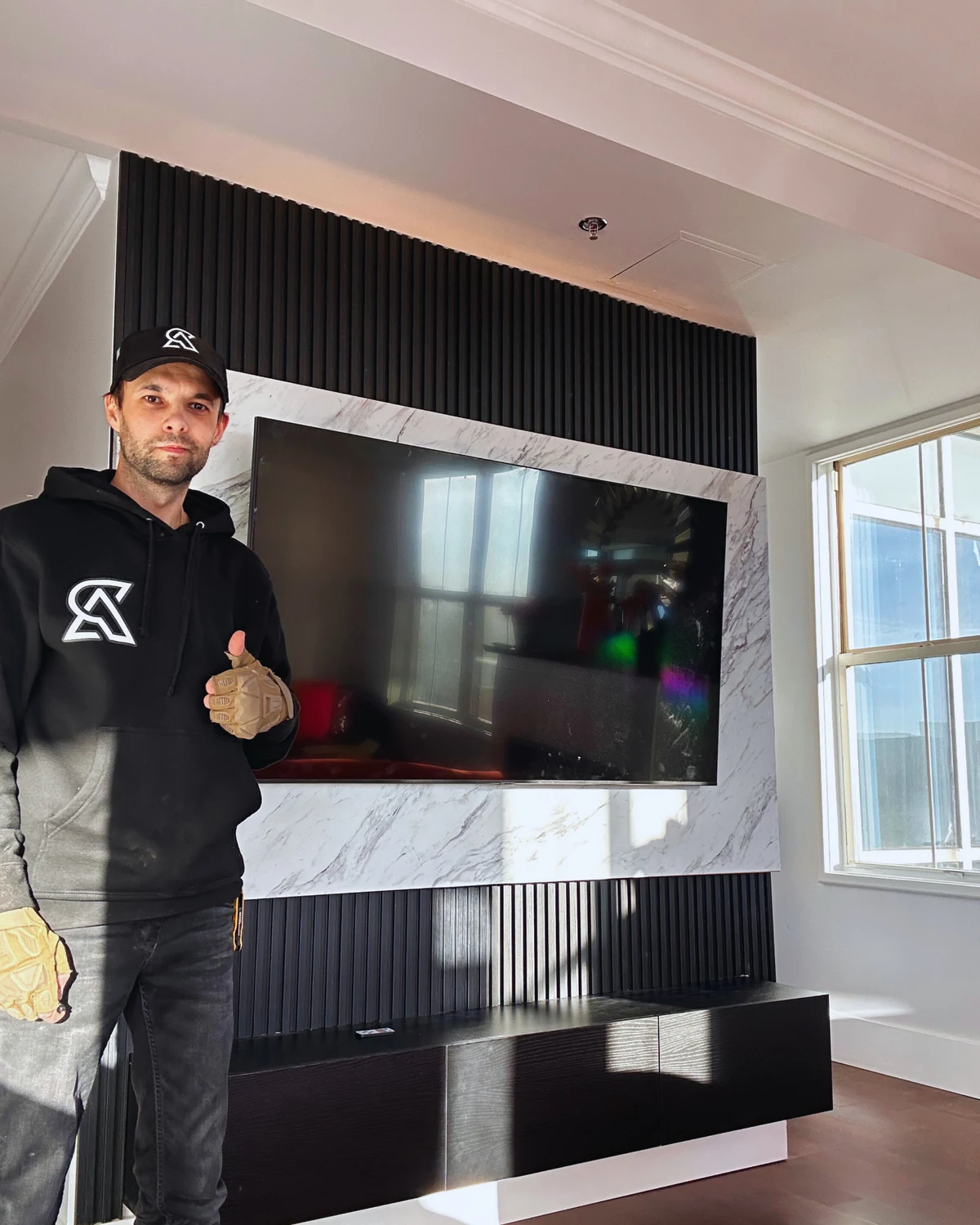 Roman beside a completed black slat TV wall with marble-look TV frame and floating console